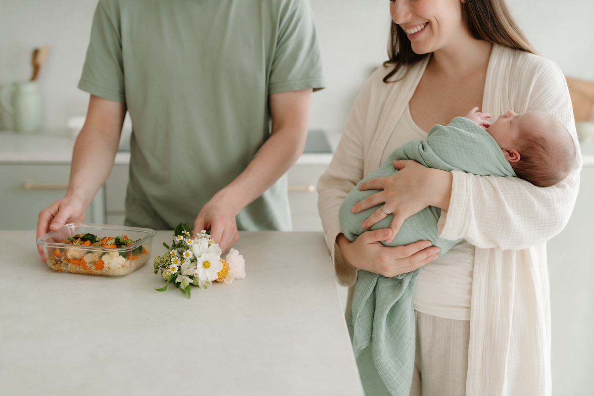 A friend bringing a home-cooked meal and flowers to a new mum holding her newborn